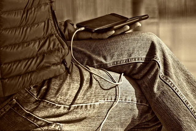 man, leg, hand, sitting, smartphone, wire, man holding smartphone, person, people, communication, technology, display, phone display, screen, brown technology, brown phone, brown mobile, brown community, brown communication, brown smartphone, brown telephone. What AI applications in creator contracts mean for sponsorship deals