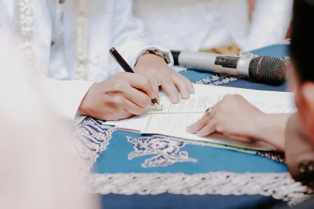 Close-up of hands signing wedding documents with microphone on table. How to read creator contracts market signals in England without a rate index