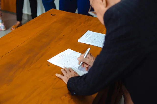 A close-up of a businessman signing official documents at a wooden desk. A UK creator sponsorship contract checklist for Scottish and Welsh deals